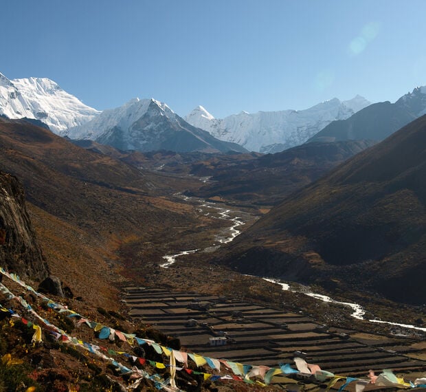 a valley with prayer flags in the foreground and snow-capped Himalayas in the distant background.
