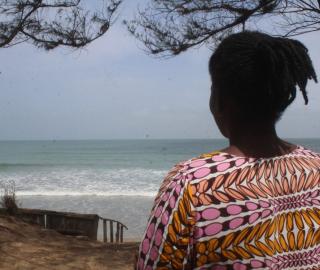 A woman looks out to the ocean from the shore. 