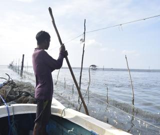 A fisher in Sri Lanka standing on a boat repairing a fishing net