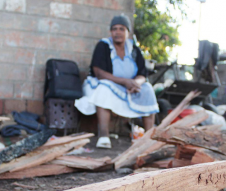 a woman sits near a pile of firewood