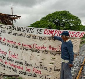 two indigenous people in mexico stand on either side of a large cloth sign during a protest