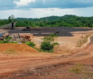 A dirt road passing by a manganese mining operation with forested area in the background.