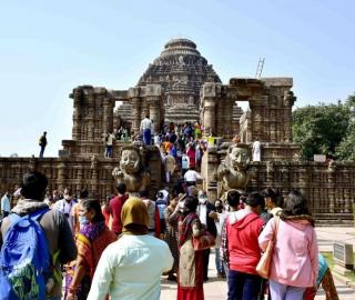 a group of people in colorful outfits stand facing away from the camera looking up at a large building temple with statues