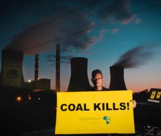 a man holding a sign that says coal kills! with a power plant behind him