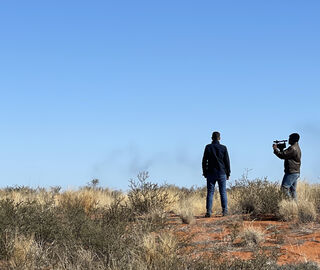 A video journalist films an interviewee and the vast landscape on a sunny day