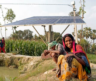 woman seated near an aquaculture pond with solar panels in background