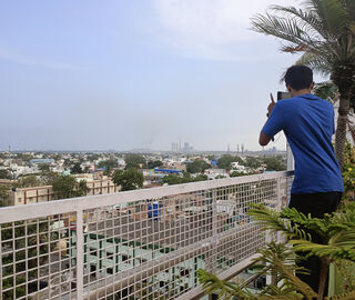 a man stands at a balcony and takes a photo of smoke from a faraway thermal power plant 