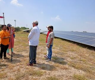 A group of people stand next to a solar energy farm.